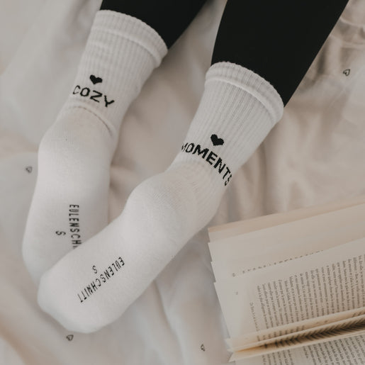 Weiße Socken „Cozy Moments“ mit Herzmotiv getragen beim entspannten Lesen im Bett