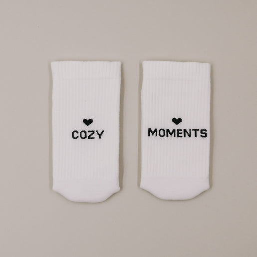 Flachliegende weiße Socken „Cozy Moments“ mit Herzsymbol und Schriftzug minimalistisch präsentiert