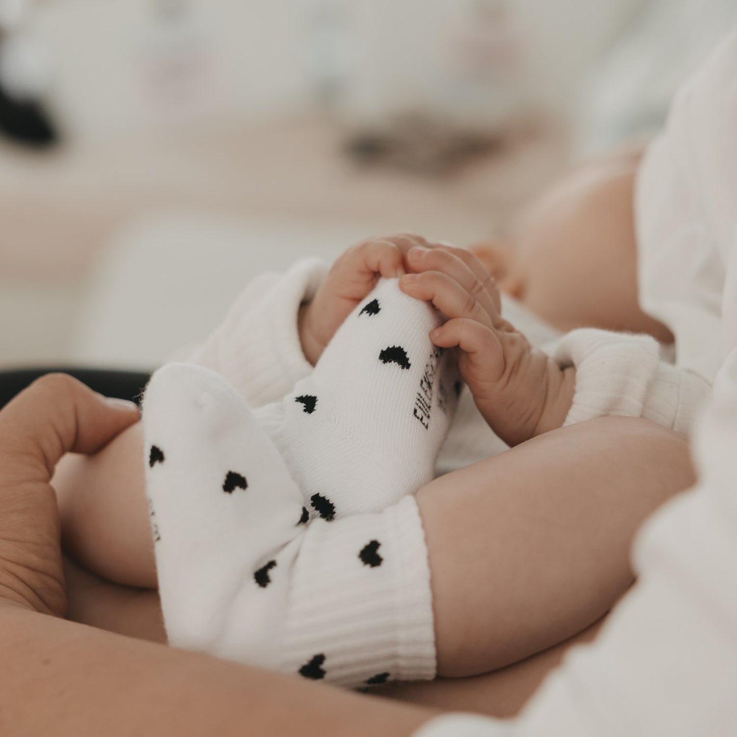 Baby greift nach eigenen Füßen, trägt weiße Socken mit schwarzen Herzen, liebevolle Szene