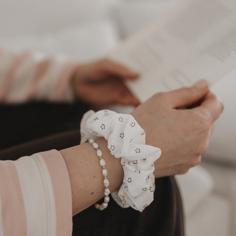 Weißes Scrunchie mit Smiley-Muster am Handgelenk getragen