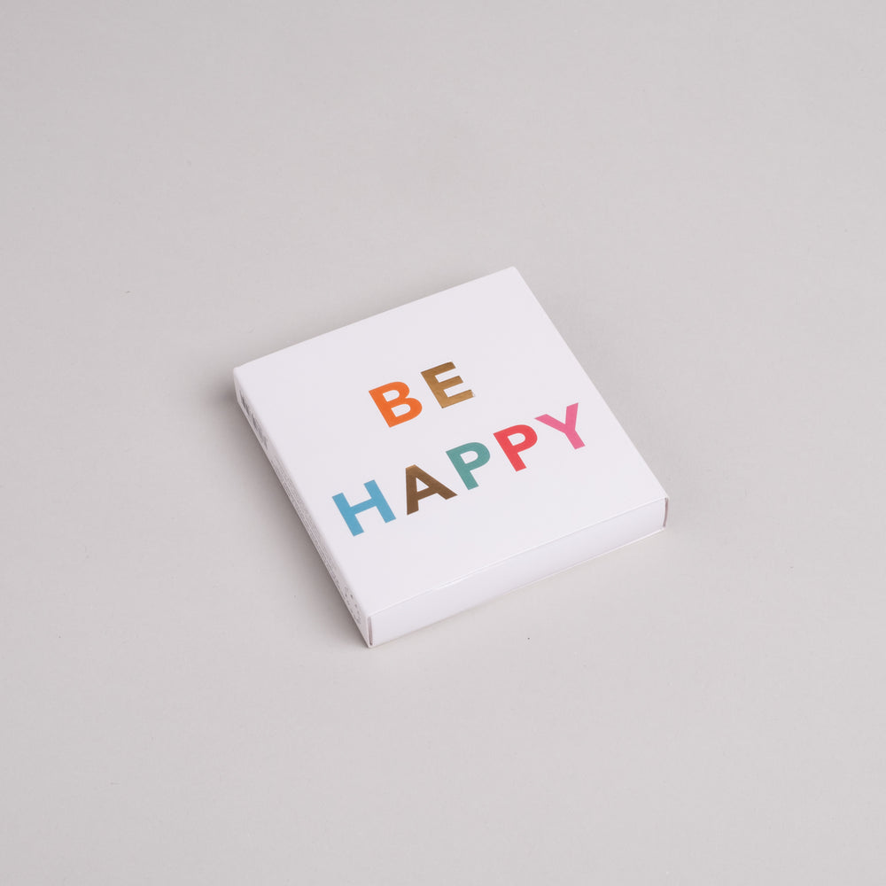 Streichholzschachtel mit bunter Aufschrift BE HAPPY auf weißem Karton, moderne Geschenkidee.