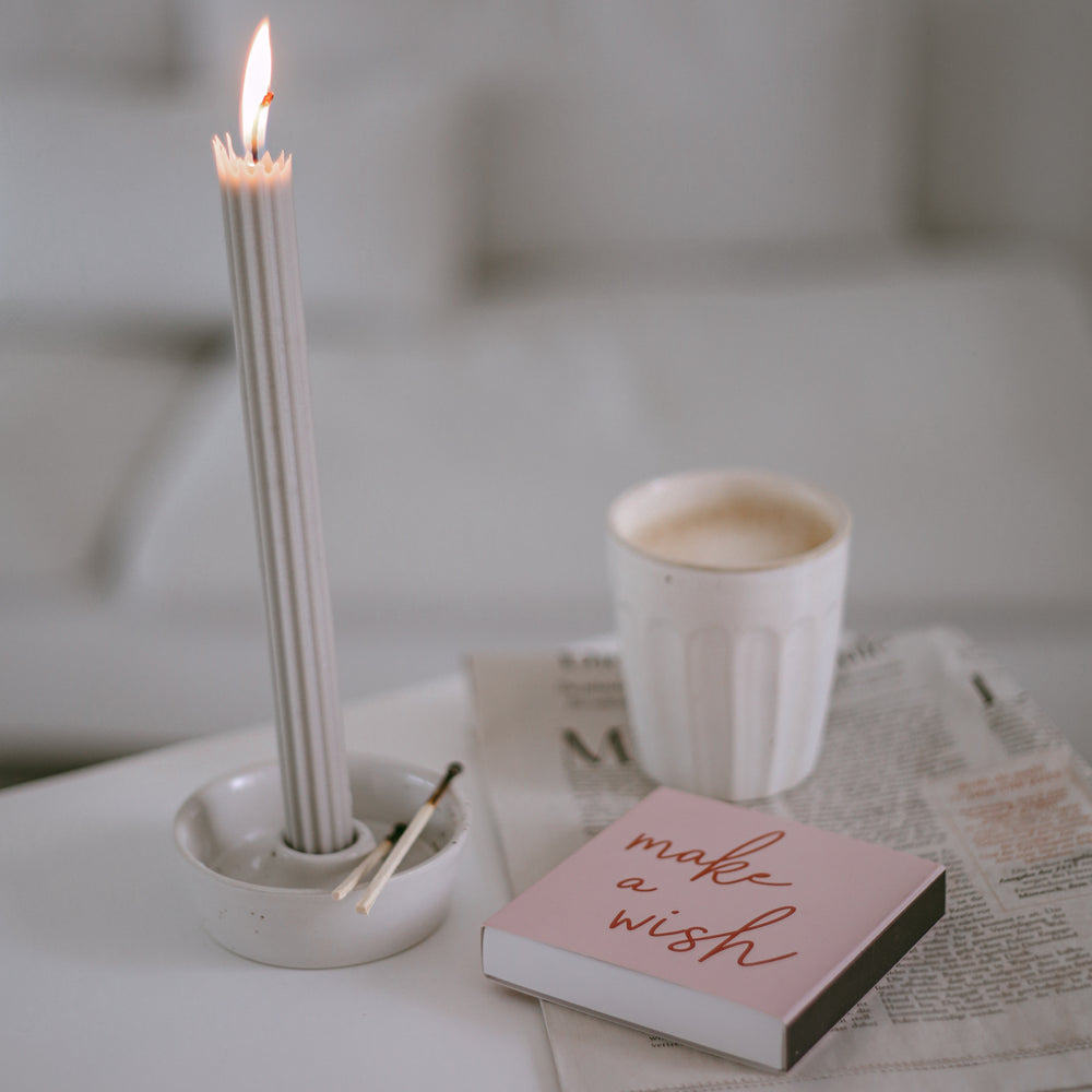 Rosa Streichholzschachtel mit Schriftzug „make a wish“ neben Kerze und Kaffee.