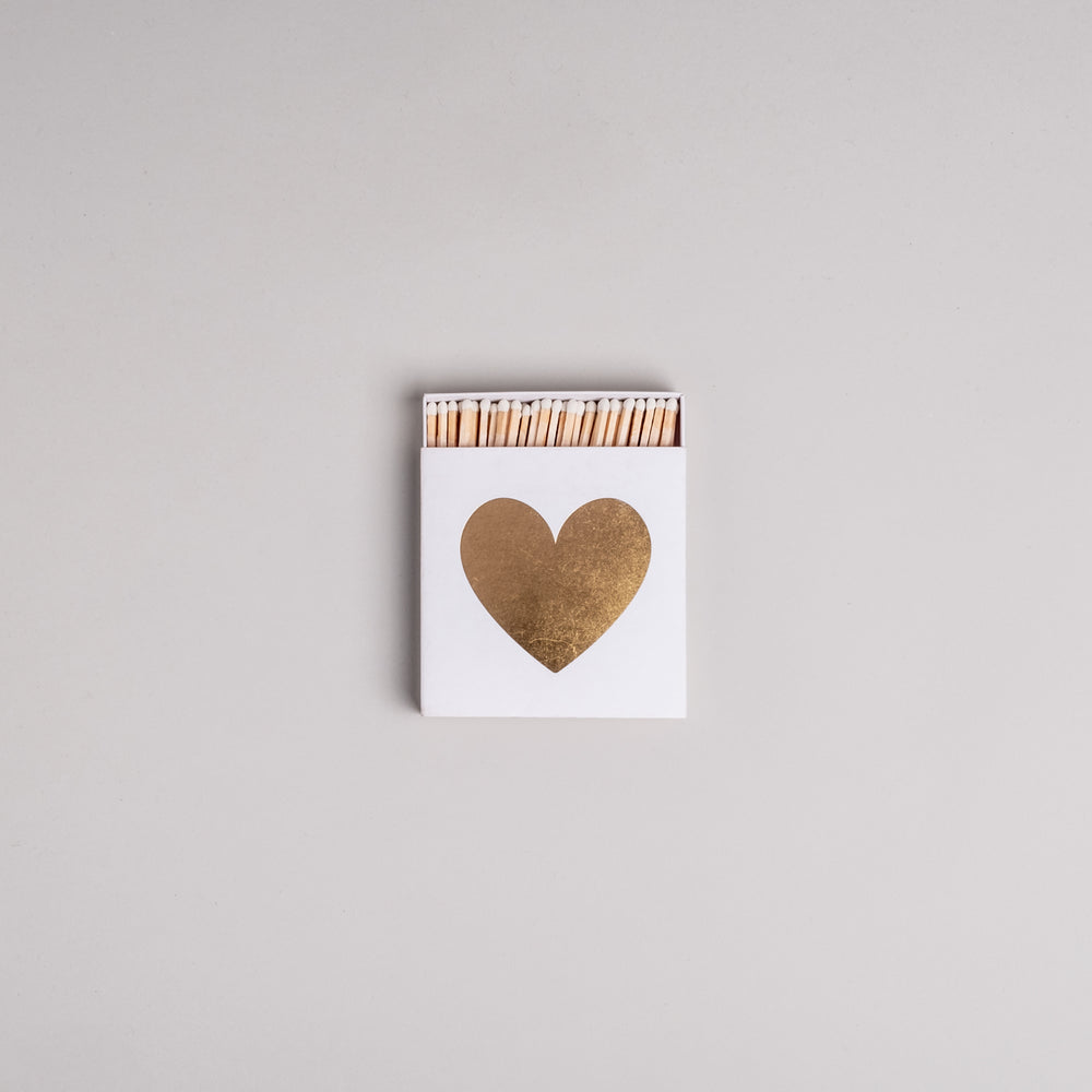 Weiße Streichholzschachtel mit goldenem Herz auf hellem Hintergrund – dekorativ und stilvoll.
