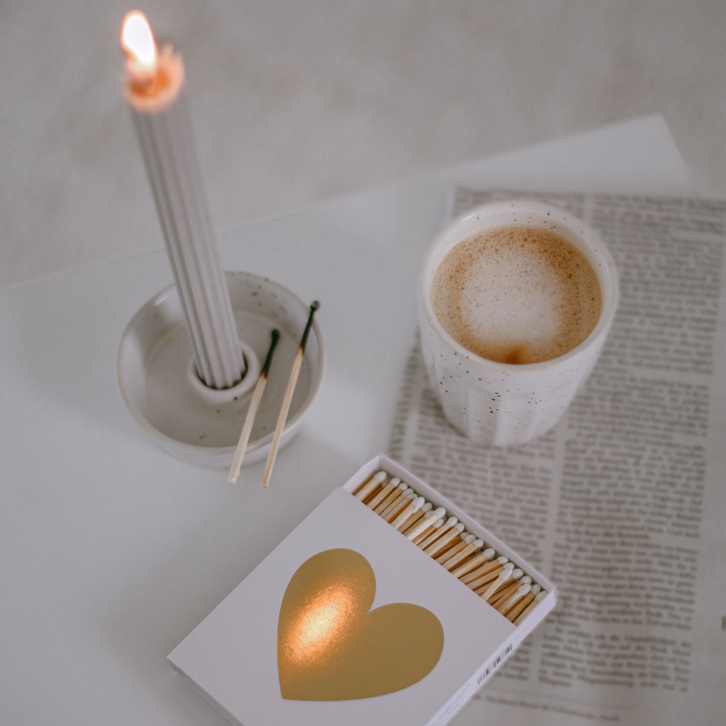 Detailaufnahme der geöffneten Streichholzschachtel mit goldenem Herz neben Kaffeebecher und Kerzenhalter.