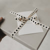 Graue Geschenkbox mit Schleife aus Geschenkband mit schwarzen Herzen.