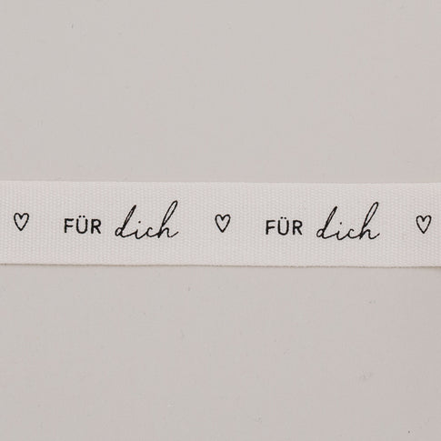 Detailaufnahme vom Geschenkband „Für dich“ mit Herzen, schwarzer Schrift auf weißem Baumwollband.