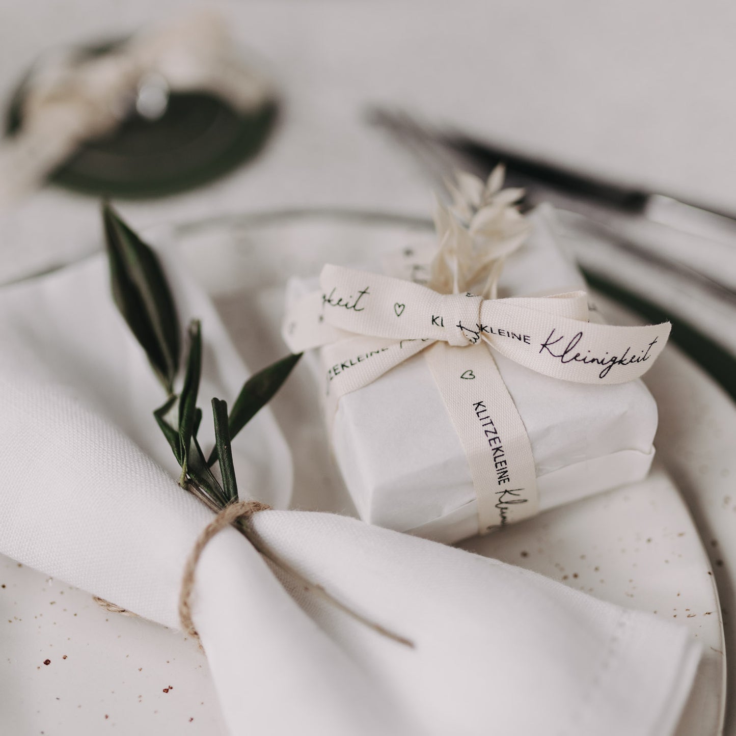 Geschenk mit weißem Geschenkband „Klitzekleine Kleinigkeit“ auf gedecktem Tisch dekoriert.