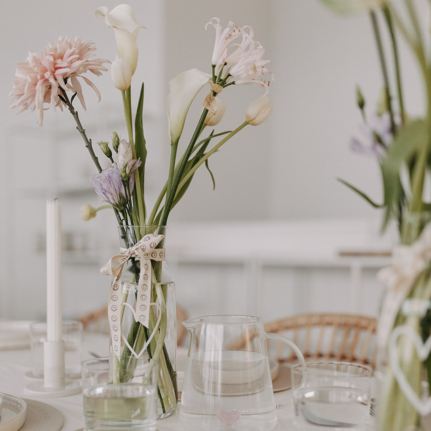 Blumenstrauß in Glasvase, dekoriert mit Smiley-Geschenkband auf festlichem Tisch.