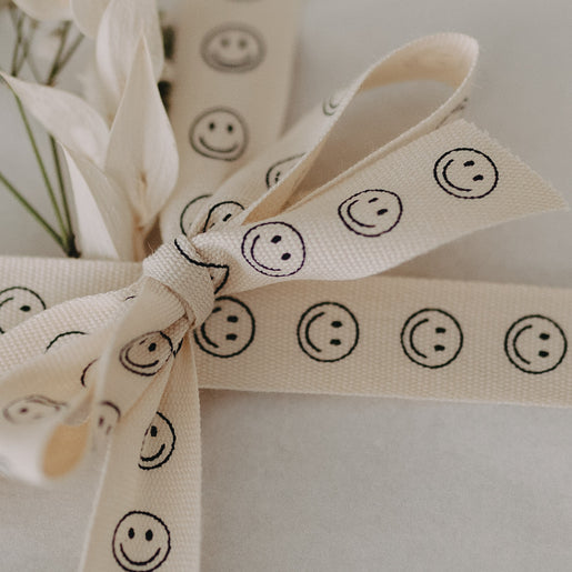 Nahaufnahme der Schleife aus Smiley-Geschenkband mit feinen Trockenblumen.