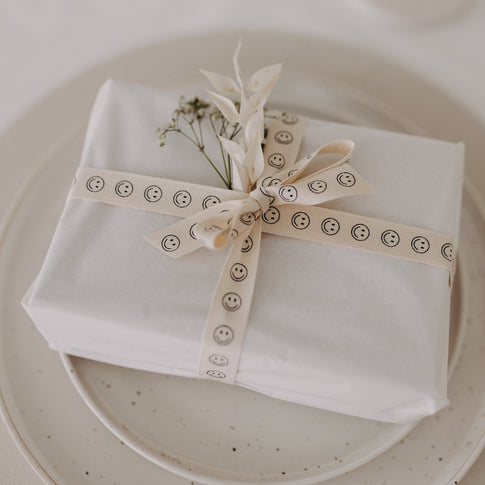 Detailaufnahme der Schleife aus cremefarbenem Geschenkband mit Smiley-Motiv.