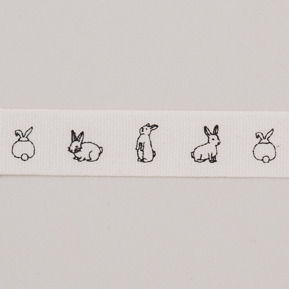 Nahaufnahme des weißen Geschenkbandes mit feinen schwarzen Kaninchenzeichnungen.