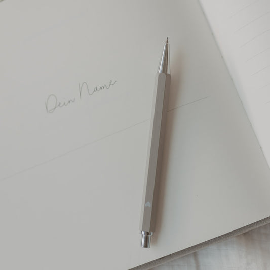 Grauer Druckbleistift auf offener Notizbuchseite mit Schriftzug ‚Dein Name‘.