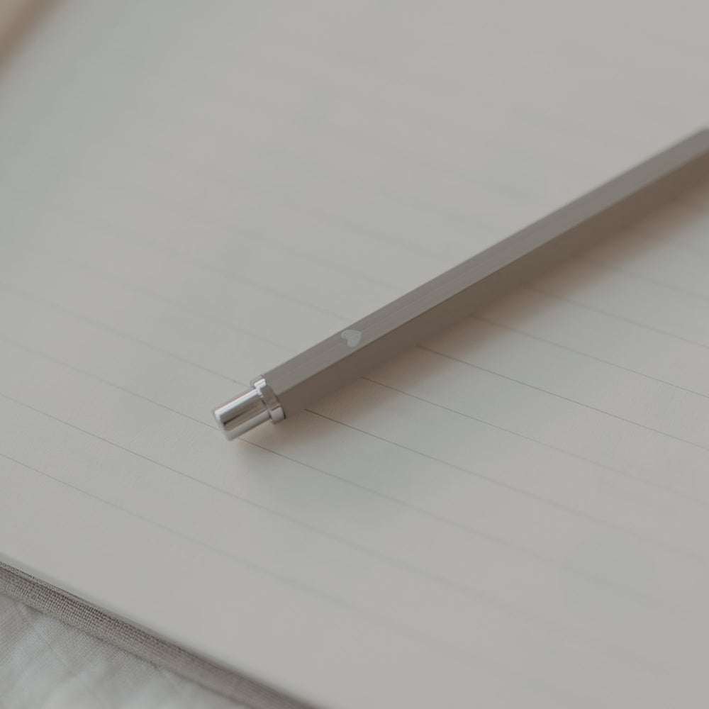 Grauer Druckbleistift auf linierten Notizbuchseiten, modernes Schreibgerät in ruhiger Szene.