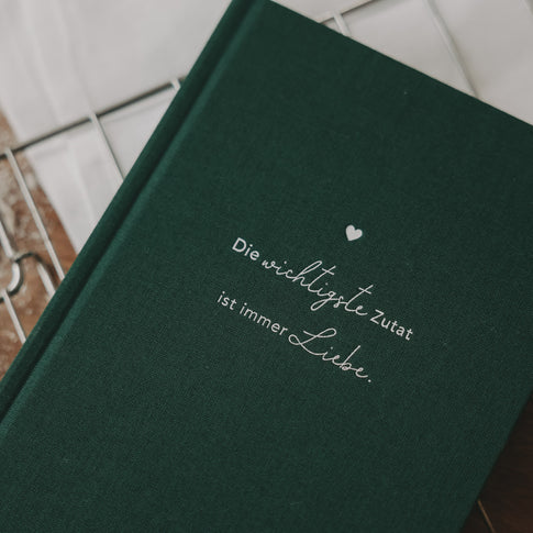Detailaufnahme des grünen Rezeptbuchs mit geprägtem Spruch „Die wichtigste Zutat ist immer Liebe“.