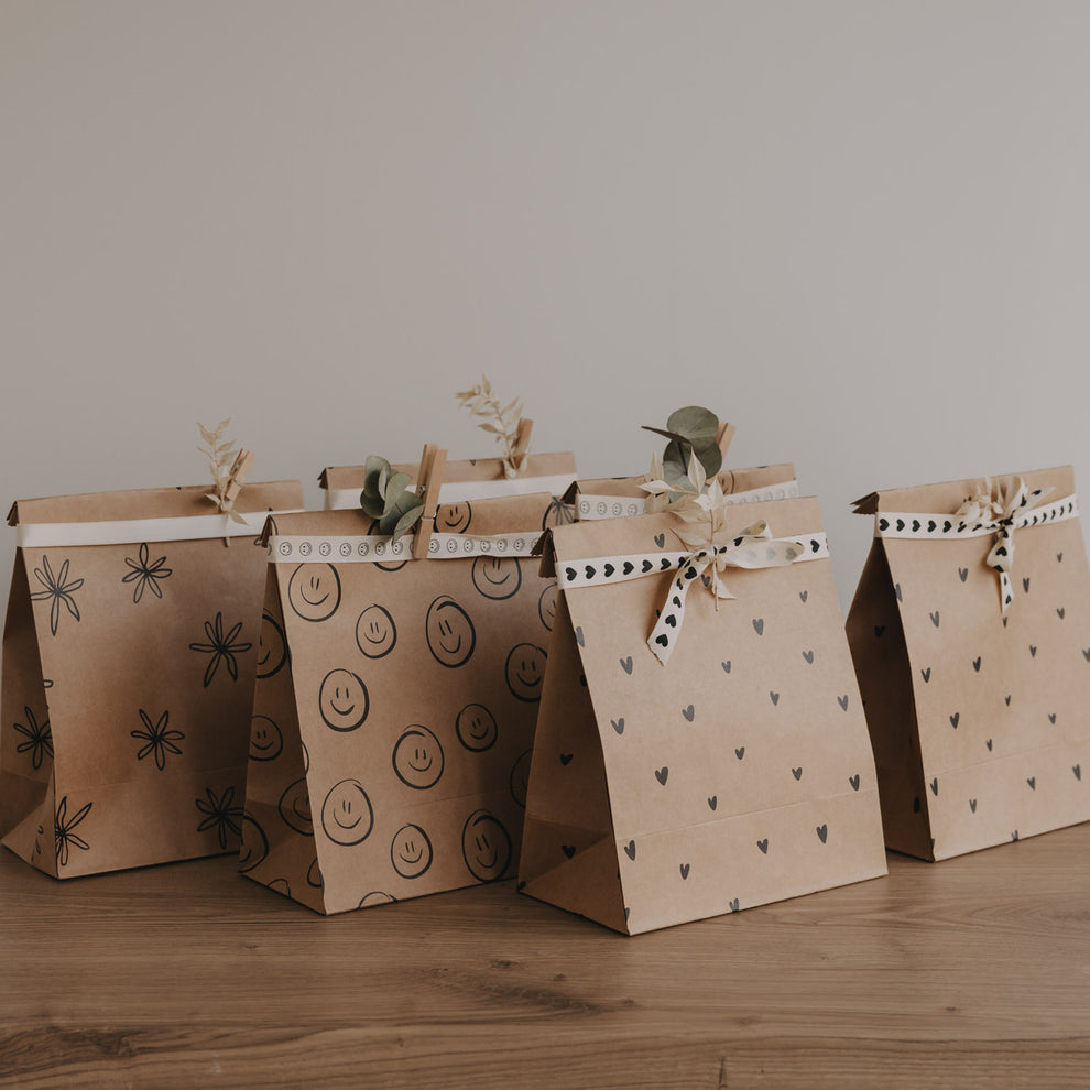 Papier Geschenktüten mit Herz-, Smiley- und Blumenmotiven im Set, dekorativ aufgereiht auf Holztisch