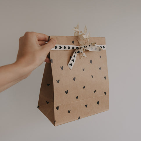 Papier Geschenktüte mit Herzmuster, Schleife und Trockenblume wird von Hand gehalten
