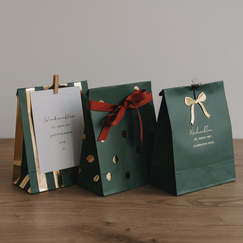 Grüne Geschenktüten aus Papier mit goldenen Akzenten und weihnachtlicher Botschaft, elegant arrangiert