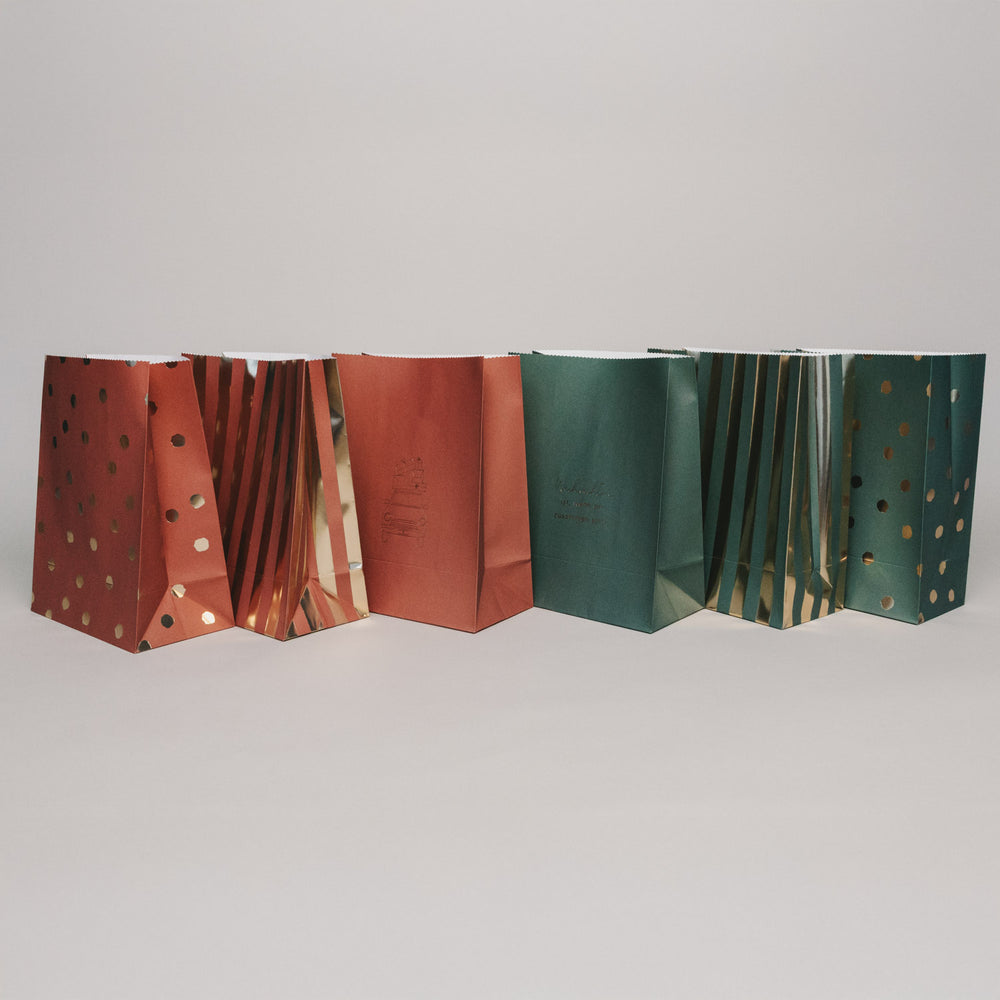 Rückansicht verschiedener Papiergeschenktüten im Weihnachtsdesign, aufgereiht vor hellem Hintergrund