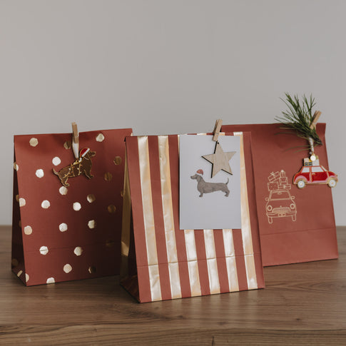 Papiergeschenktüten zu Weihnachten in Rostrot mit Punkten, Streifen und Illustration, dekorativ aufgestellt