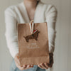 Person hält weihnachtliche Kraftpapier-Geschenktüte mit „Frohe Weihnachten“ und Dackel-Anhänger