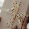 Detailansicht einer Schleife aus beigem Geschenkband mit schwarzen Herzen