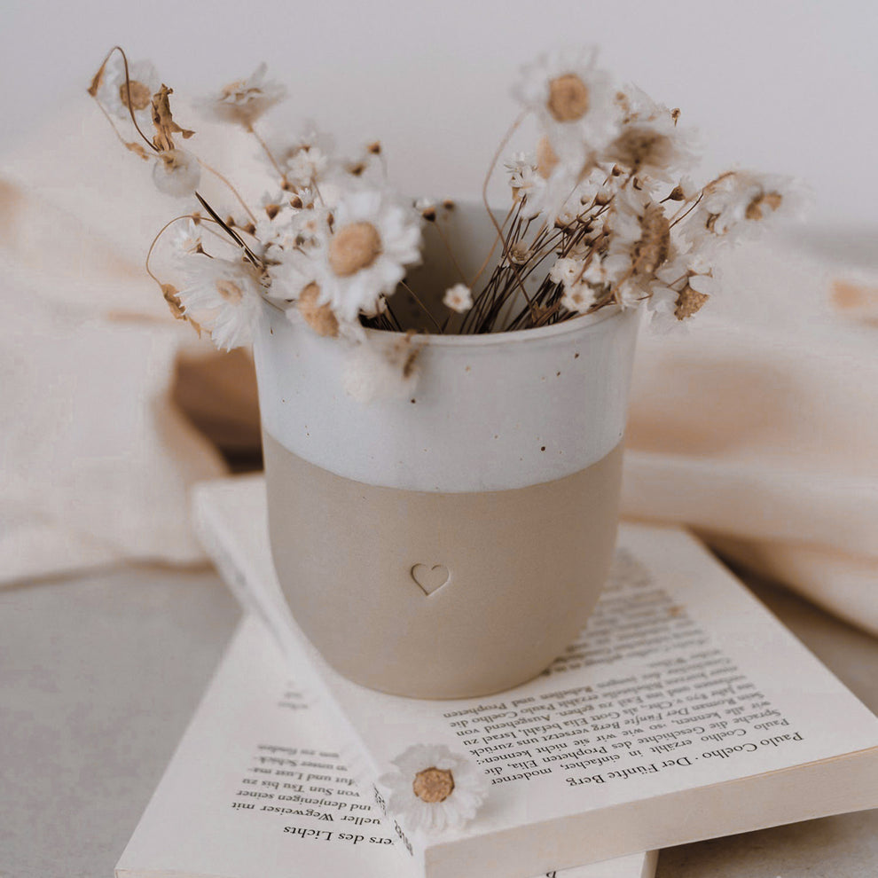 Becher Herz auf Buch mit Gänseblümchen – zartes Styling für gemütliche Momente.